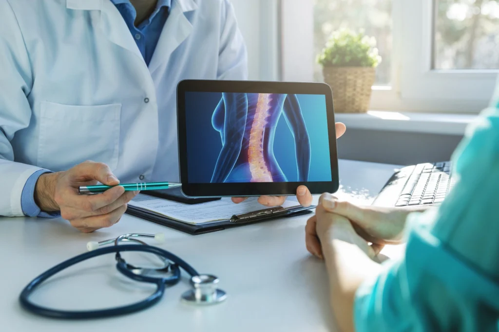 A doctor showing to a patient a tablet with an image of an x-ray model of a female body with the spine being highlighted.