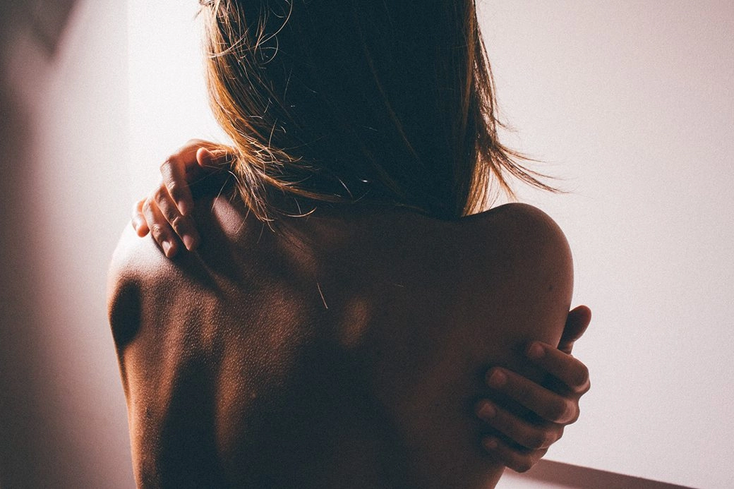 A woman wrapping her arms around her, touching the sides of her back.