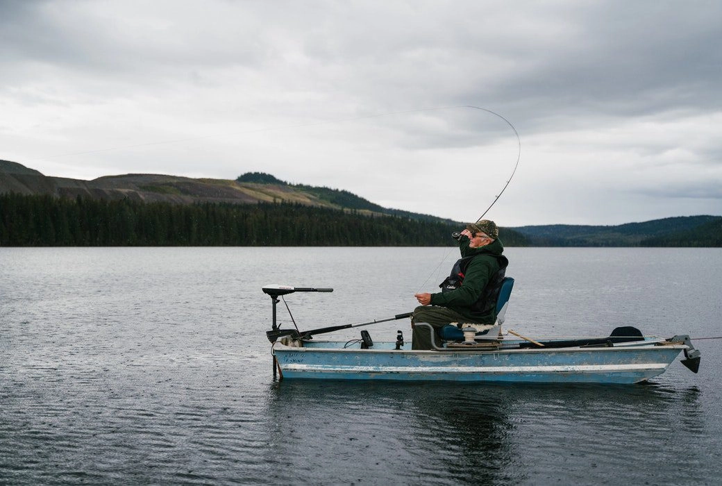 A man fishing on a small boat in a lake.