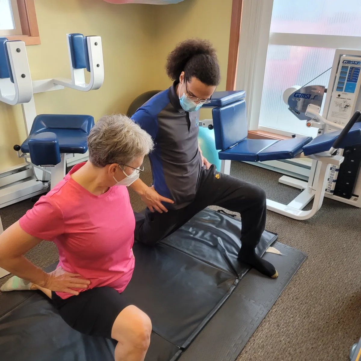 Performing hip and thigh physical therapy stretches with a patient with lower back pain.