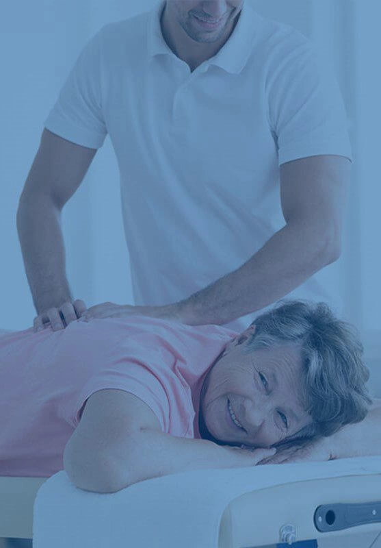 An elderly woman lying on a massage table having her back treated by a chiropractor and looking happy.