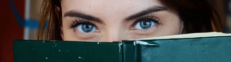 A woman showing her eyes behind a book.
