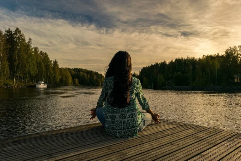 A woman meditating in a pier in front of the sea.