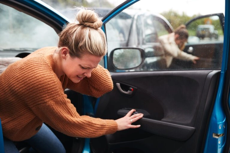A woman trying to exit a car feeling pain in her neck.