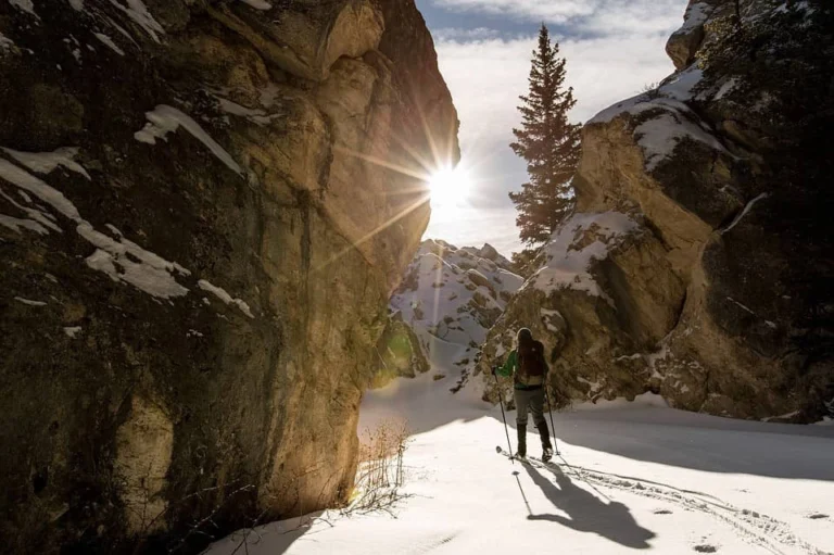 A person skiing near boulders against the sunlight.