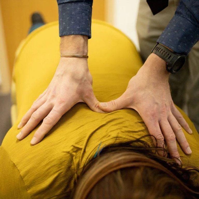A woman lying face down on a massage table and having her upper back treated by a chiropractor.