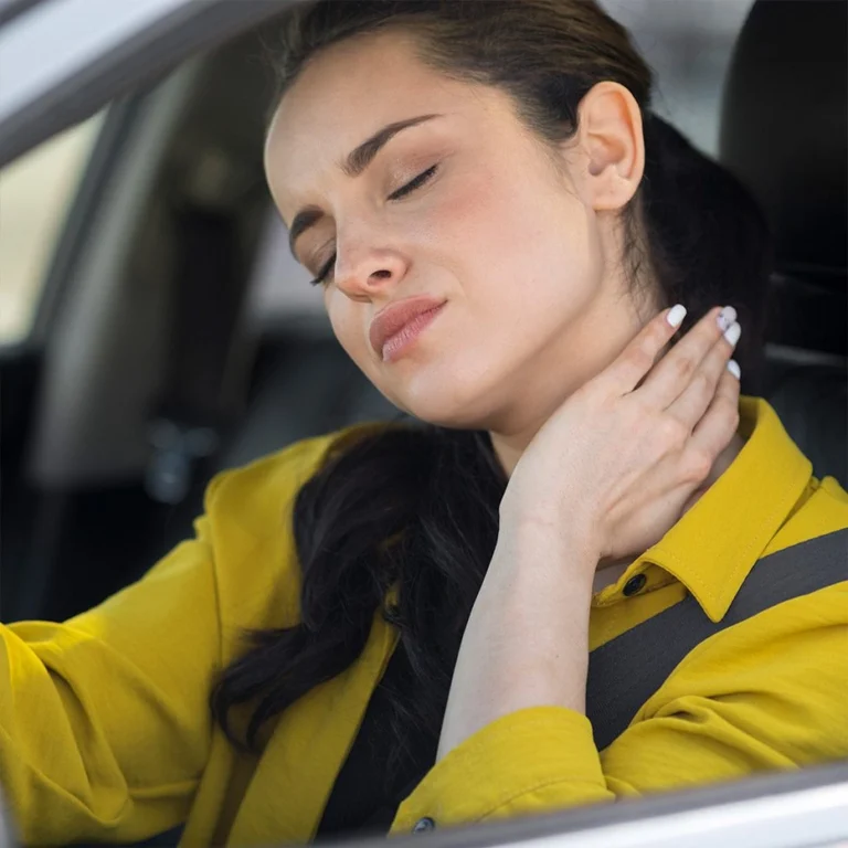 A woman touching her neck while sitting in a car in pain.