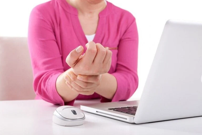 A woman feeling carpal pain in front of a laptop.