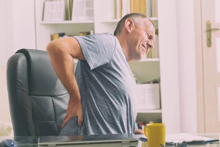 A sitting man touching his lower back in pain.