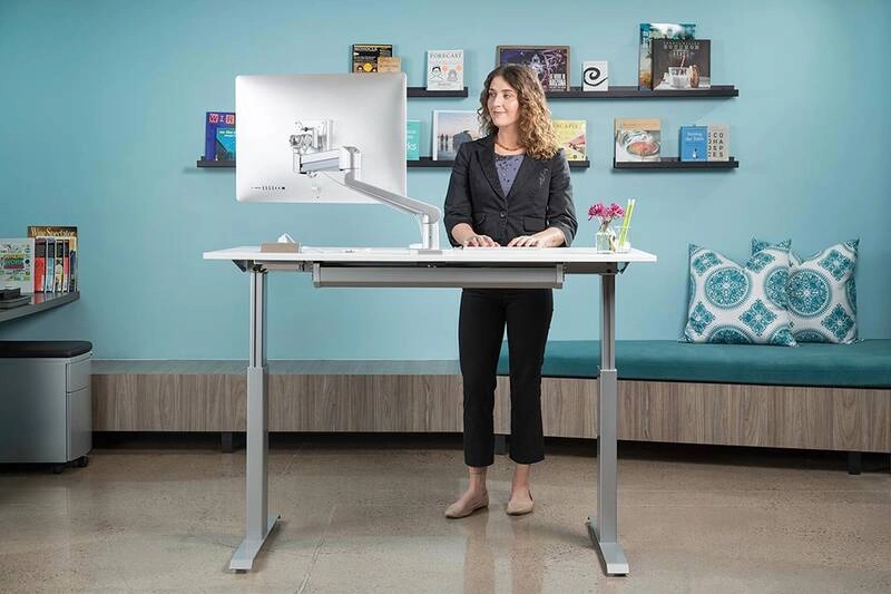 A woman working with a computer on a standing desk.