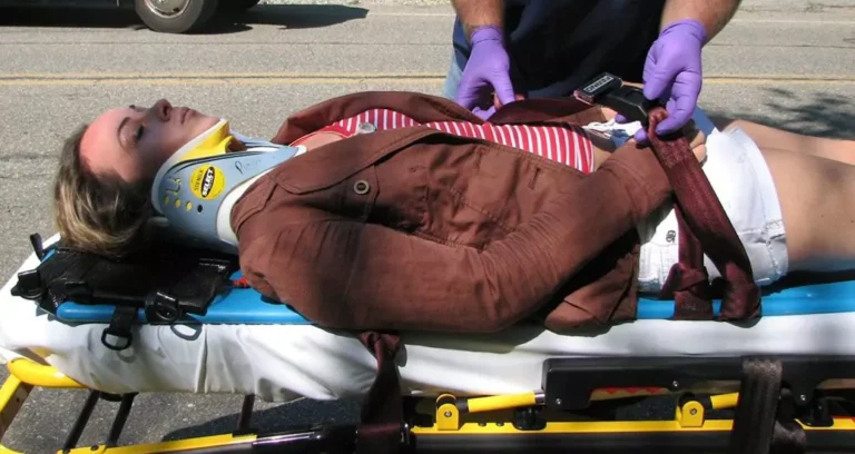 A woman with neck collar on an ambulance stretcher.