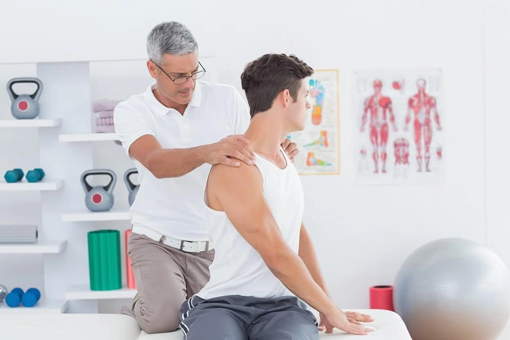 A young man siting on a massage table and being examined by a chiropractor