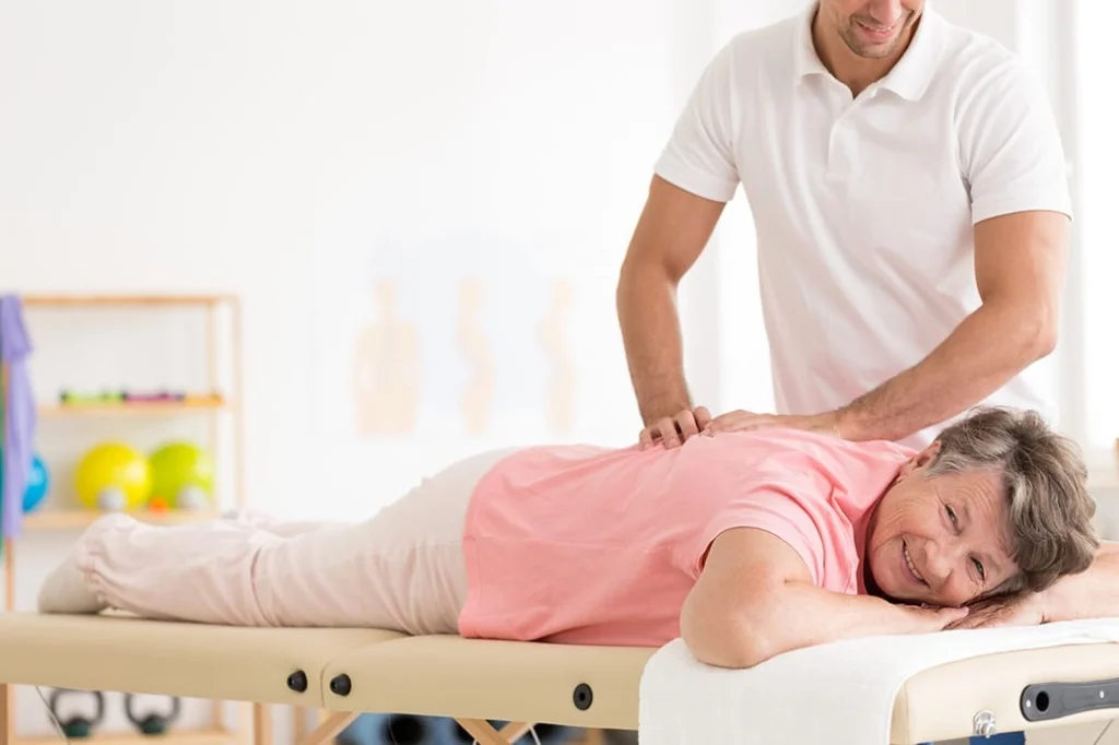 An elderly woman being treated by a chiropractor on her back and looking happy.