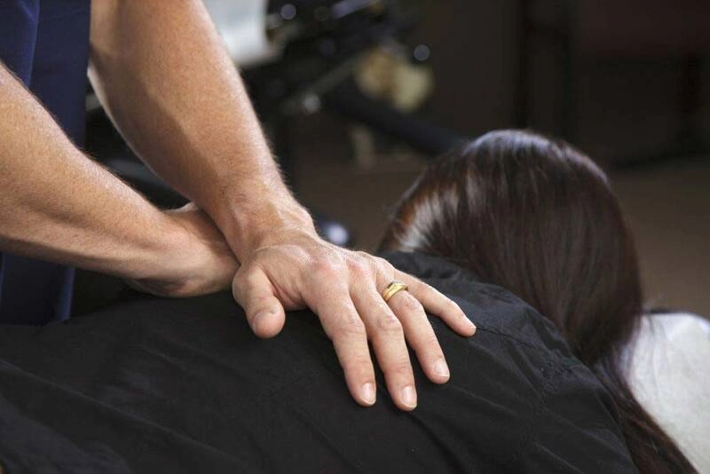 A chiropractor applying pressure to a woman's upper back.
