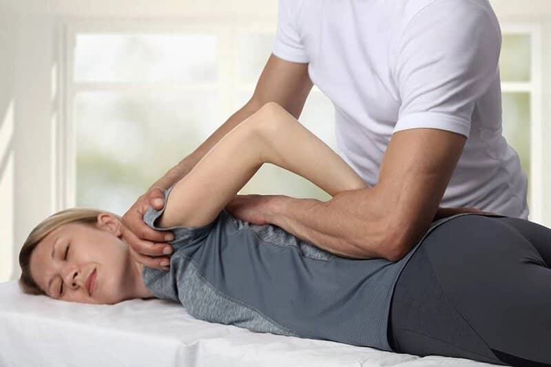 A woman having her shoulder stretched by a chiropractor while lying on a massage table.