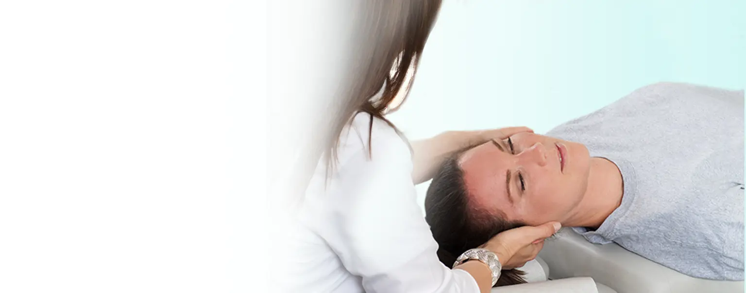 A woman lying on her back and getting treated in the neck by a chiropractor.