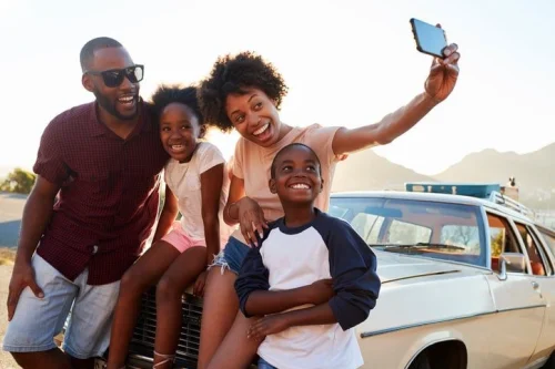 A family of four having a group photo in front of a car.
